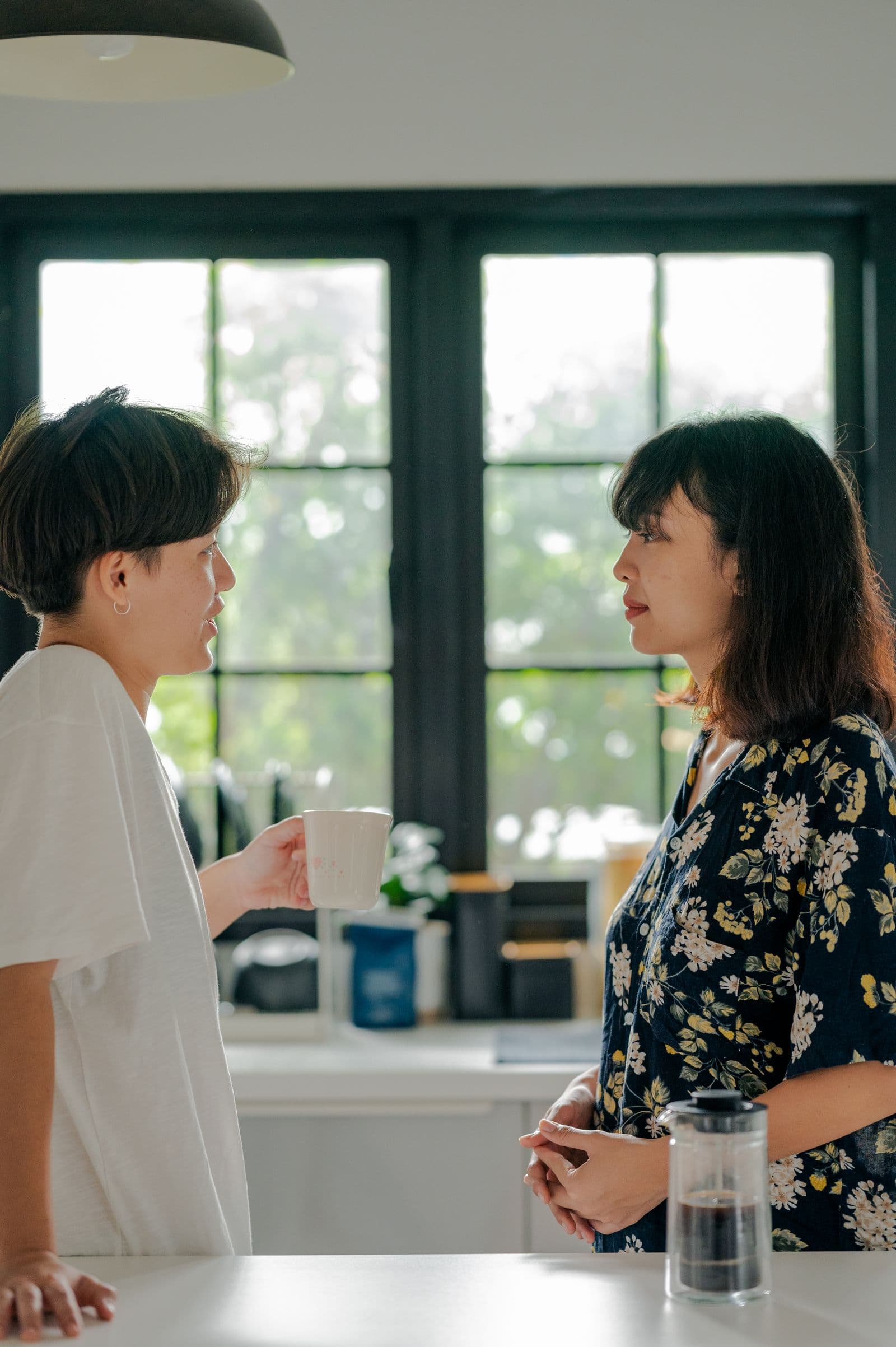 Two people talking over coffee by a window in natural light